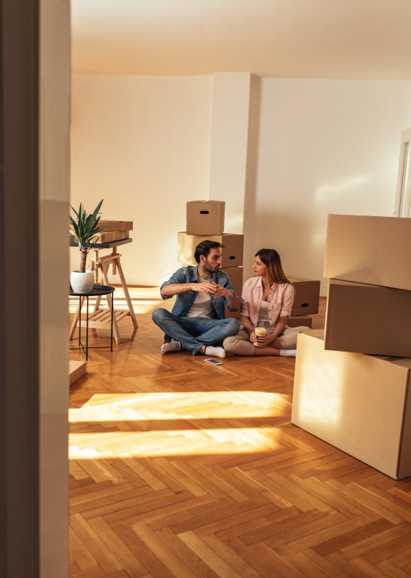 Happy young couple sitting on the floor in their new home and taking a rest while surrounded by boxes
